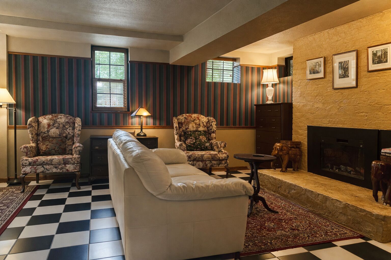 A living room with a checkered floor, striped wallpaper, a fireplace, and two armchairs.