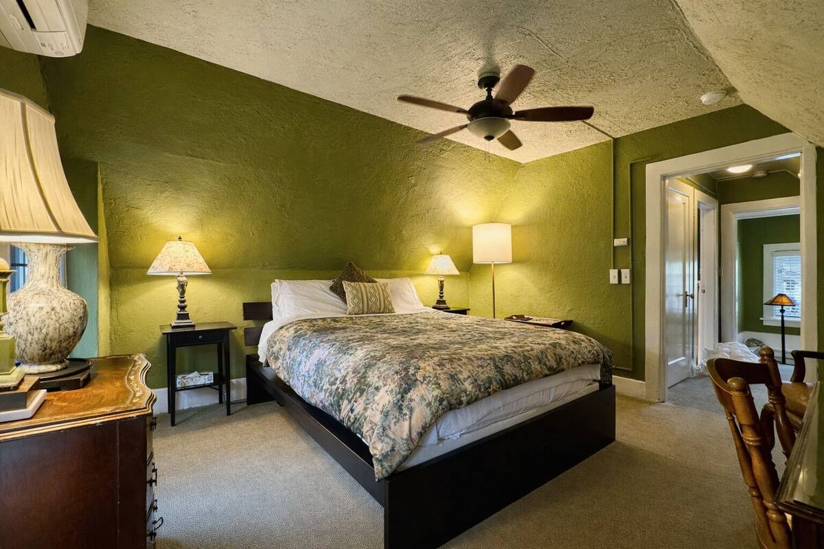 Un dormitorio con cama, dos lámparas de noche, un ventilador de techo y una mesita de noche.