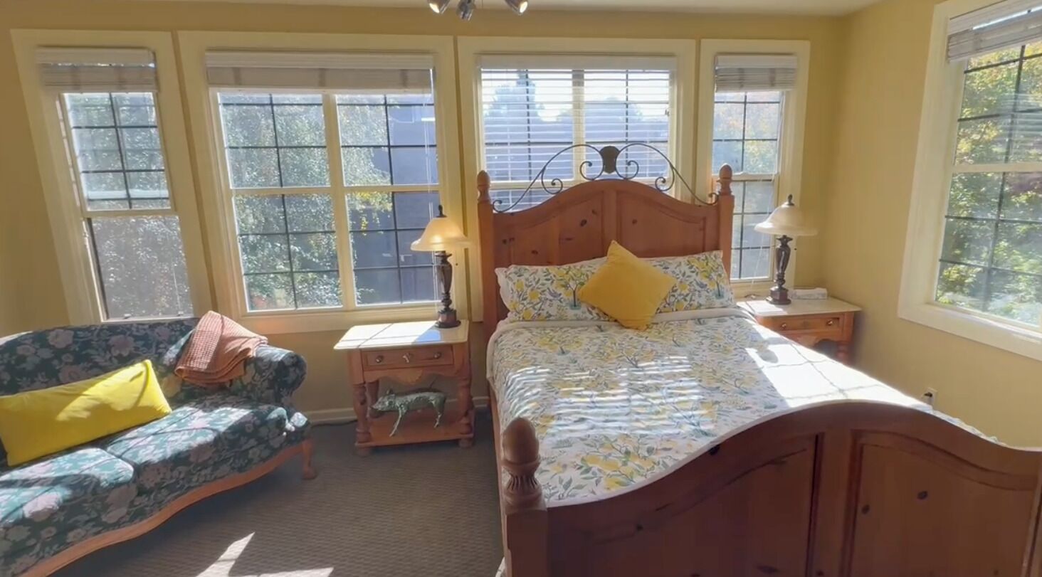 A bedroom with a bed, a nightstand, a lamp, a sofa, and a window.
