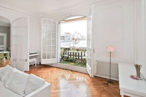 A spacious room with a large open door leading to a balcony, a white sofa, a radiator, and a pink floor lamp. - 200-square-meter luxury apartment on a quiet, private street. Downtown Paris (PARIS)