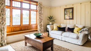 A living room with a wooden bench, a white sofa, and a large window with curtains. - Family-friendly, well-equipped, spacious country house,garden and Fibre Internet (Ohoka)