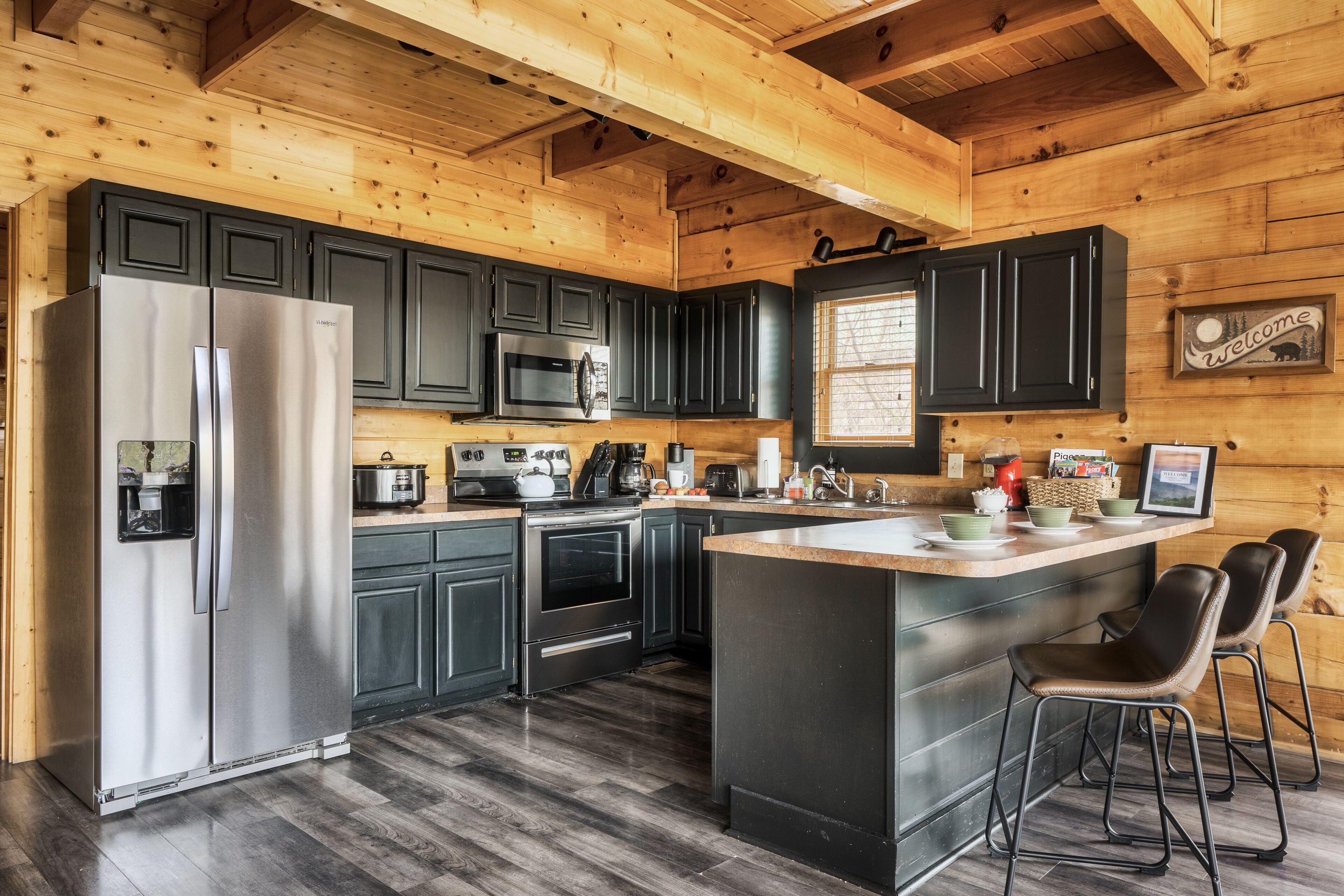A modern kitchen with dark cabinets, stainless steel appliances, and a wooden ceiling.