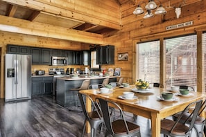 A wooden cabin kitchen with a central island, black cabinets, stainless steel appliances, and a dining area with chairs and a table set for four.