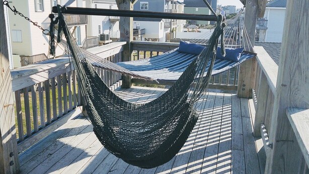 Un hamac suspendu à une terrasse en bois, avec en arrière-plan la vue sur des bâtiments.