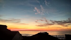 Une vue sur le coucher de soleil en bord de mer, avec des bâtiments se détachant en silhouette sur le ciel.
