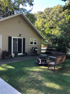 Een gelijkvloers huis met een veranda, een klein terras en een achtertuin met een barbecue en tuinmeubilair.