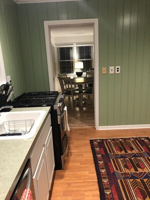 Una cocina con estufa, lavamanos y un comedor con mesa y sillas.