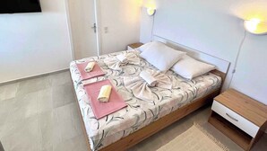 Et soveværelse med seng, natbord, fjernsyn og to vægmonterede lamper.