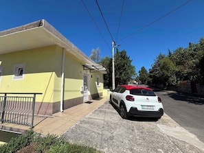 Un edificio amarillo con un coche blanco estacionado frente a él, una barandilla metálica y un cielo azul despejado.
