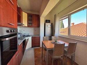 Une cuisine compacte dotée de meubles en bois, d’un four encastré, d’un réfrigérateur et d’un coin repas avec une table et des chaises.
