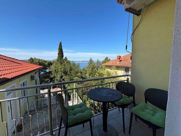 A balcony with a table and chairs, a railing, and a view of buildings and trees. - Holiday apartment mit Meerblick (Dramalj)