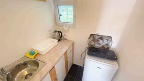 Uma cozinha compacta com pia, chaleira, torradeira e uma pequena geladeira.