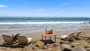 A beach with lounge chairs and a table with a bottle and basket.