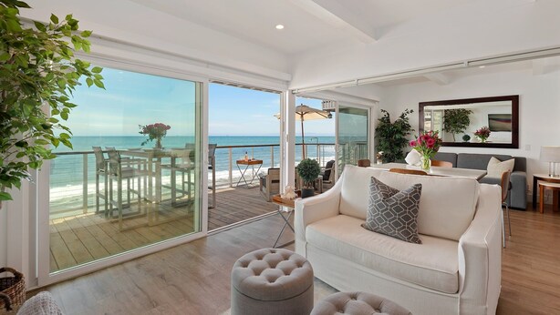 A spacious living room with a large sliding glass door leading to a balcony with a view of the ocean.
