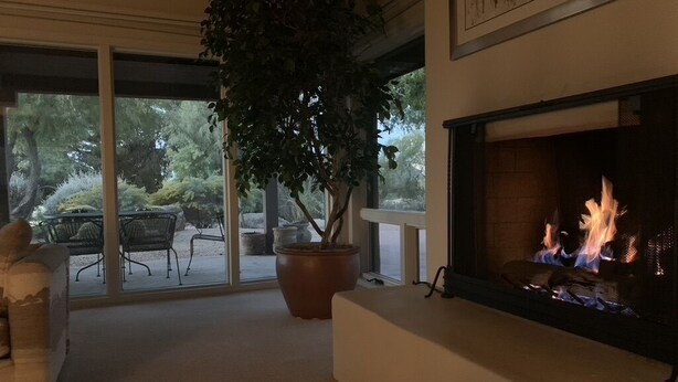A living room with a fireplace, a large potted plant, and a view of the outdoors through large windows. - Perfect Home for Super Bowl & Waste Management Open in Boulders on the N. Course (Carefree)