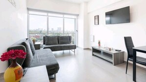 Ein modernes Wohnzimmer mit einem grauen Sofa, einem Esstisch und einem an der Wand befestigten Fernseher.