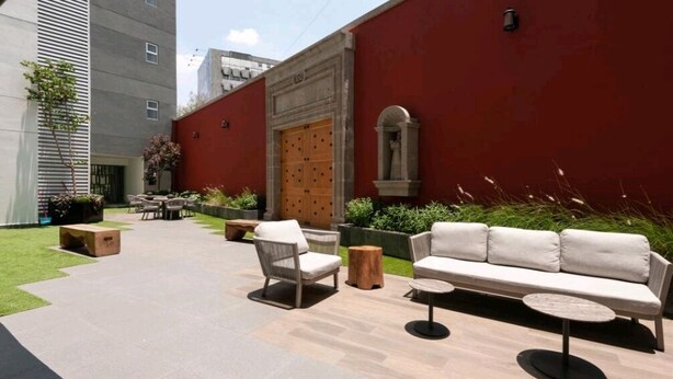Ein Patio im Freien mit roter Wand, einer Holztür und Gartenmöbeln, darunter eine Couch und Stühle.