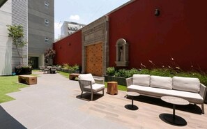 An outdoor patio area with a red wall, a wooden door, and outdoor furniture including a sofa and chairs.
