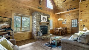 A cozy log cabin interior with a stone fireplace, wooden furniture, and a dining area. - Awesome deals, King bed, Hot Tub, Private, Arcade, Real log cabin (Sevierville)