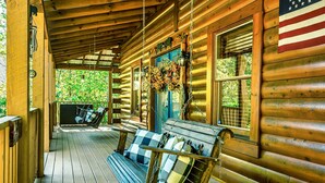 A wooden cabin with a porch, a swing chair, and a hanging flower arrangement. - Awesome deals, King bed, Hot Tub, Private, Arcade, Real log cabin (Sevierville)