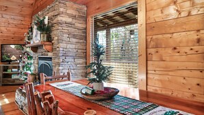A wooden interior with a stone fireplace, a Christmas tree, and a dining table with a placemat. - Awesome deals, King bed, Hot Tub, Private, Arcade, Real log cabin (Sevierville)