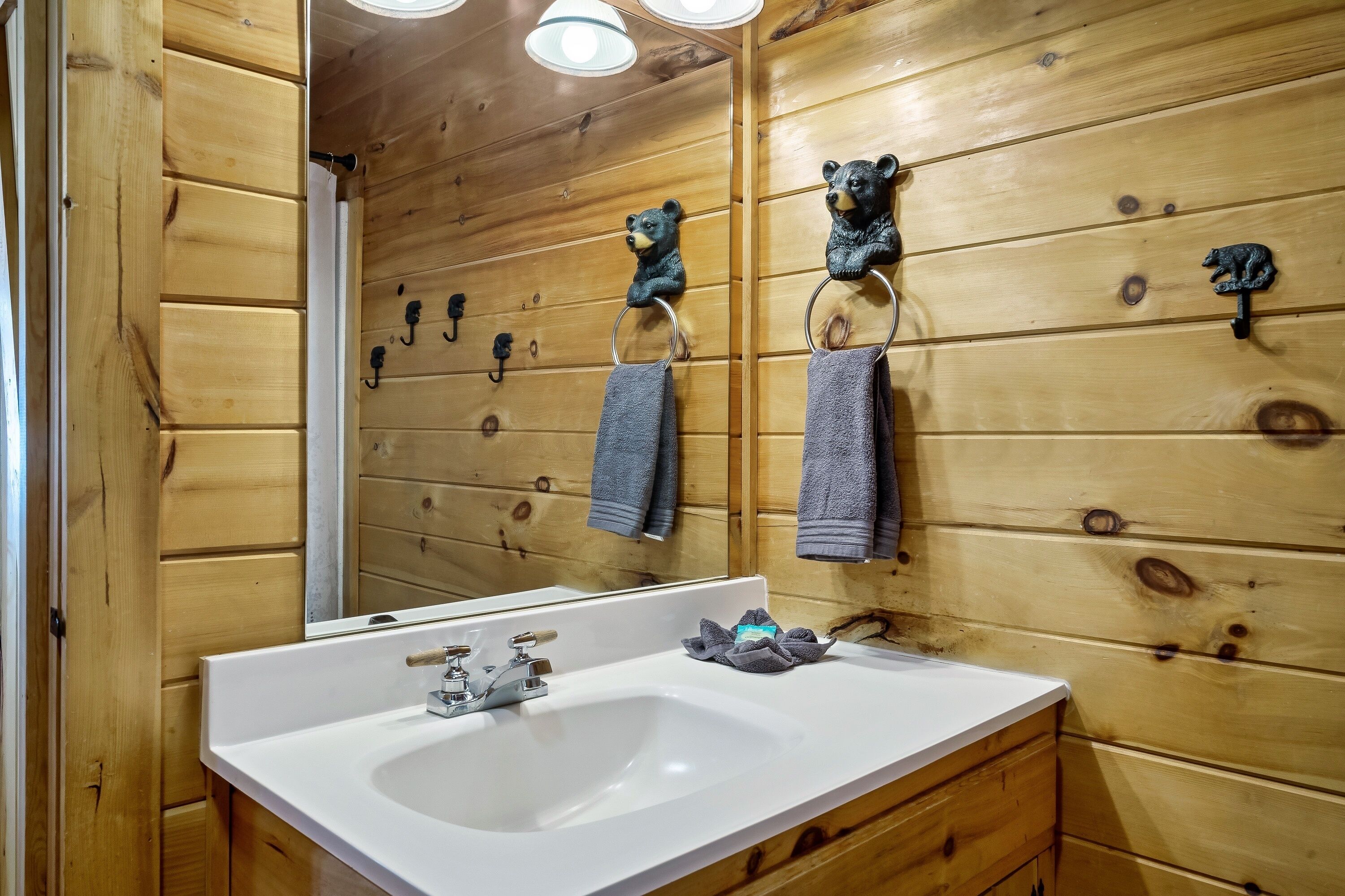 A wooden cabin bathroom with a white sink, two towel rings with towels, and a mirror reflecting the wooden walls.
