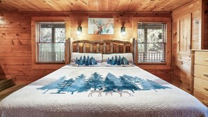 A log cabin bedroom with a bed featuring a forest-themed bedspread, two wall-mounted lights, and a ceiling fan. - Awesome deals, King bed, Hot Tub, Private, Arcade, Real log cabin (Sevierville)