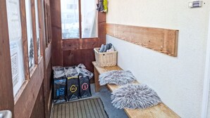 Un pasillo estrecho con paredes de madera, una ventana, un estante de madera con paraguas, una cesta con toallas y bolsas en el suelo.