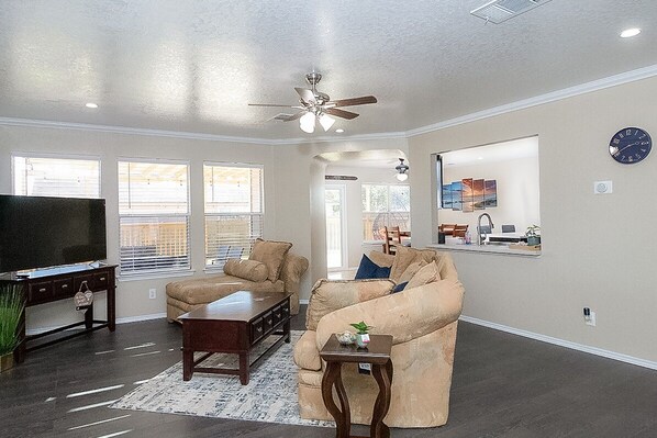 A spacious living room with a large flat-screen TV, two beige sofas, a coffee table, and a ceiling fan. - Cozy 3BR Retreat w/Amazing Outdoor Deck Near Randolph AFB & JBSA Ft. Sam Houston (Converse)