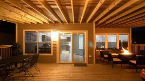 An outdoor deck with a wooden ceiling, a dining table with chairs, and a fire feature.
