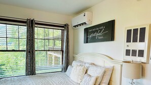 Ein Schlafzimmer mit einem großen Bett, einem Fenster mit Vorhängen, einer Klimaanlage, einem an der Wand befestigten Schild und einem Nachttisch mit Lampe.