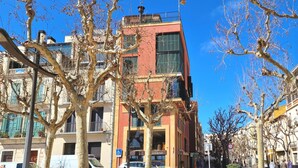 A multi-story building with balconies, a parking area with cars, and a clear blue sky.