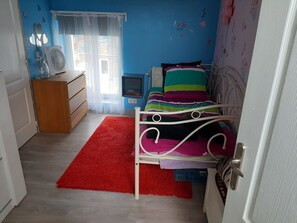 Quarto com cama, penteadeira, mesa pequena, janela com cortinas e radiador.