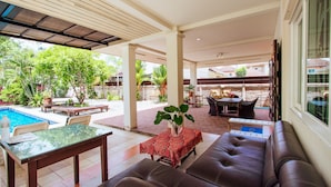 Area patio esterna con piscina, posti a sedere e una zona coperta con tavolo e sedie.