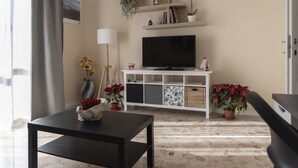 Una sala de estar con televisor, estantes con plantas, lámpara y una mesa.