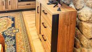 A room with a stone wall, wooden furniture, a television, and a patterned rug. - Private cottage near Tykocin (Tykocin)