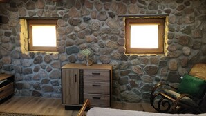 A room with stone walls, wooden beams, a wooden cabinet, a green chair, and two windows. - Private cottage near Tykocin (Tykocin)
