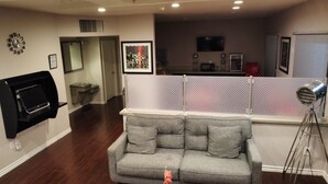 A living room with a grey sofa, a mounted TV, a wall clock, and a patterned partition.