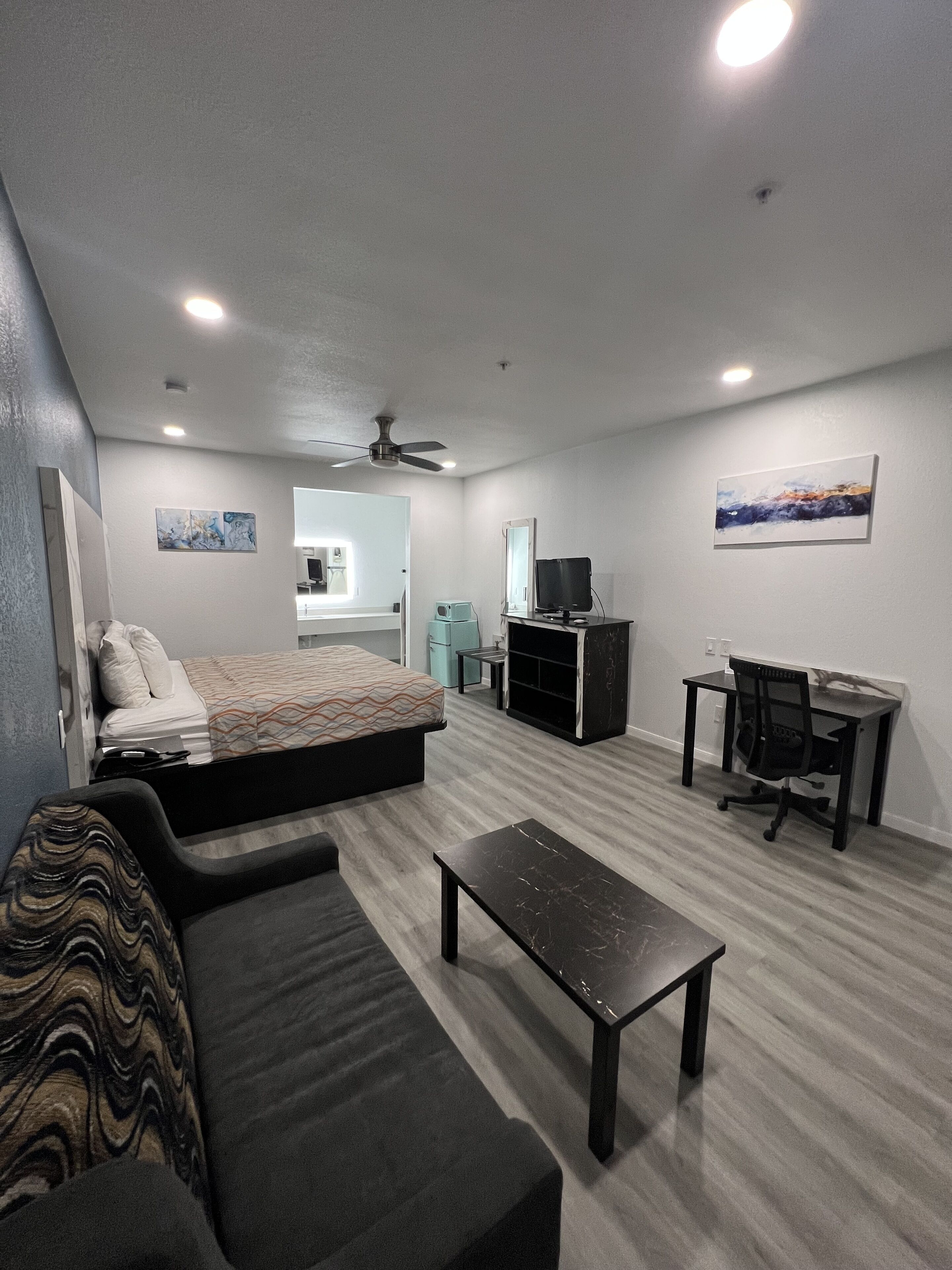 A modern, well-lit room with a bed, a sofa, a desk, and a television.