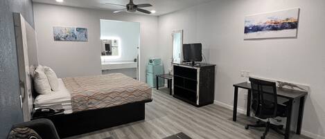A modern, well-lit room with a bed, a sofa, a desk, and a television.