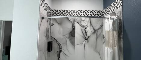 A bathroom with a glass-enclosed shower, a white bathtub, and a patterned tile border.