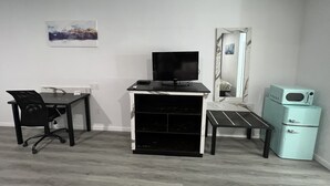 A room with a desk, chair, TV, microwave, and a mirror.
