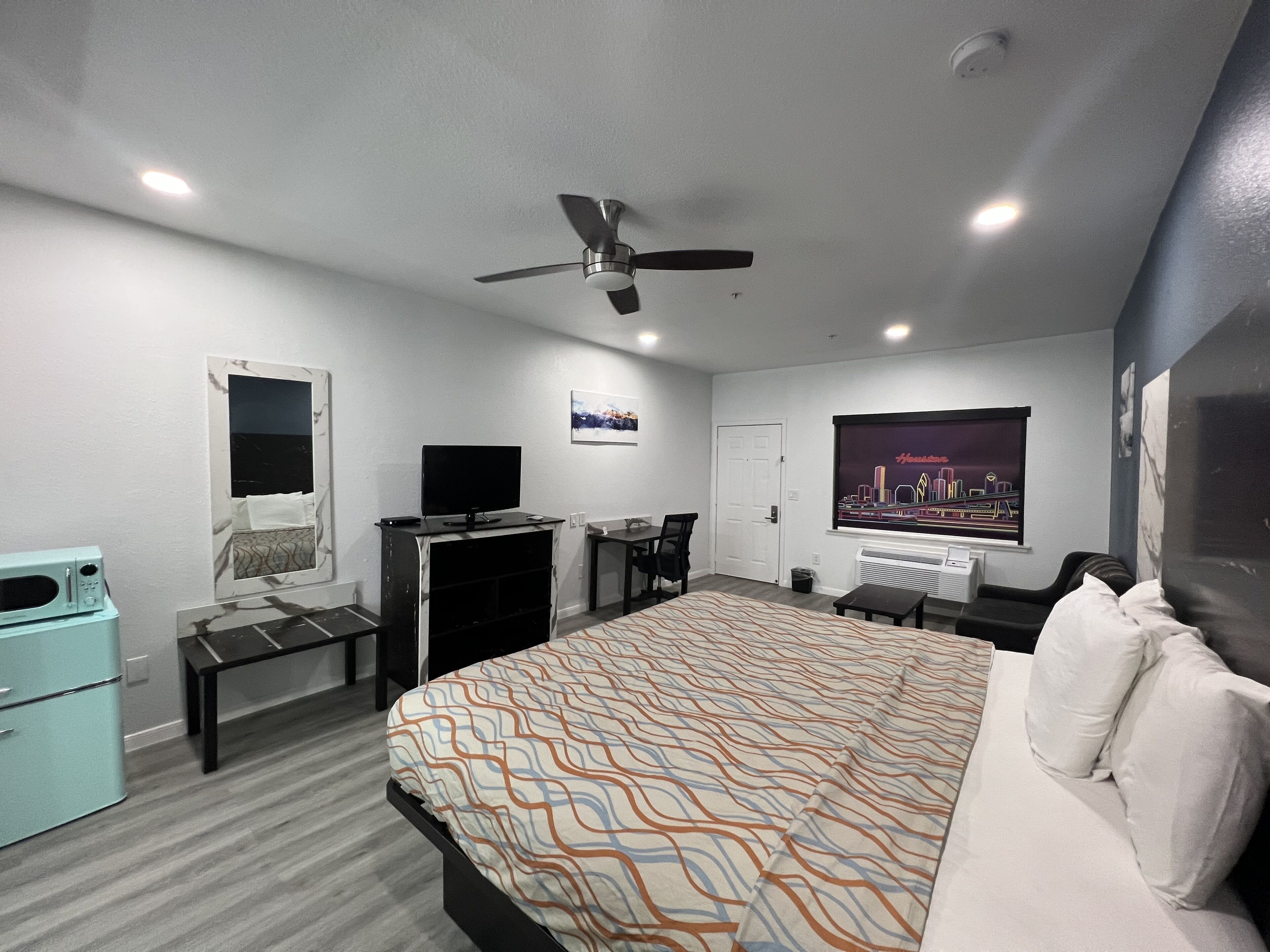 Une chambre d’hôtel moderne équipée d’un grand lit, d’un bureau, d’une chaise, d’une télévision et d’un ventilateur de plafond.