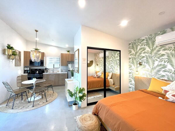 Eine moderne, kompakte Wohnung mit einer Küchenzeile, Essbereich und einem Schlafzimmer mit einem großen Bett und Blick durch eine Schiebetür.