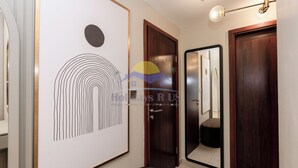 A hallway with a framed artwork, a wooden door, and a mirror reflecting a room with a bed and a nightstand. - Holidays R Us villa 3 bedroom premium location (Dubai)