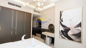 A bedroom with a large wardrobe, a bed with white linens, a modern chandelier, and a large abstract painting. - Holidays R Us villa 3 bedroom premium location (Dubai)