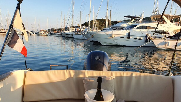 A boat with a cushioned seating area, a bottle of champagne, and a glass on a small table. - UNUSUAL NIGHT ABOARD A BOAT (Saint-Florent)