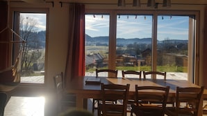 Ein Essbereich mit großem Fenster, Holztisch, Stühlen und hängenden Pendelleuchten.