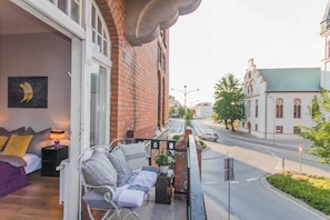 Un balcon avec un canapé, une plante en pot et une vue sur une rue bordée d’immeubles et de voitures.
