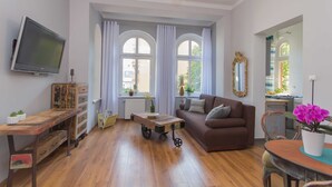 Una sala de estar con un sofá, televisor, una mesa de madera y una ventana con cortinas.